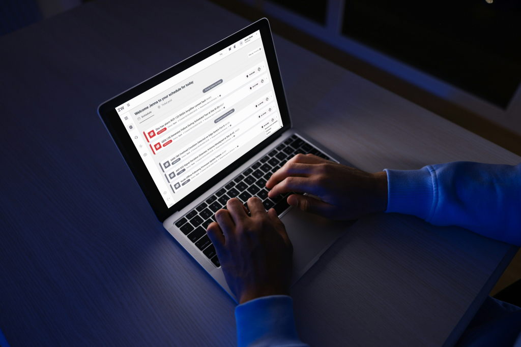 Person typing on a laptop displaying the FieldMate AI Assistant app with message categories, seated at a desk in a dimly lit room.